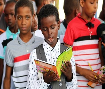 A boy reading a book with other children beside him