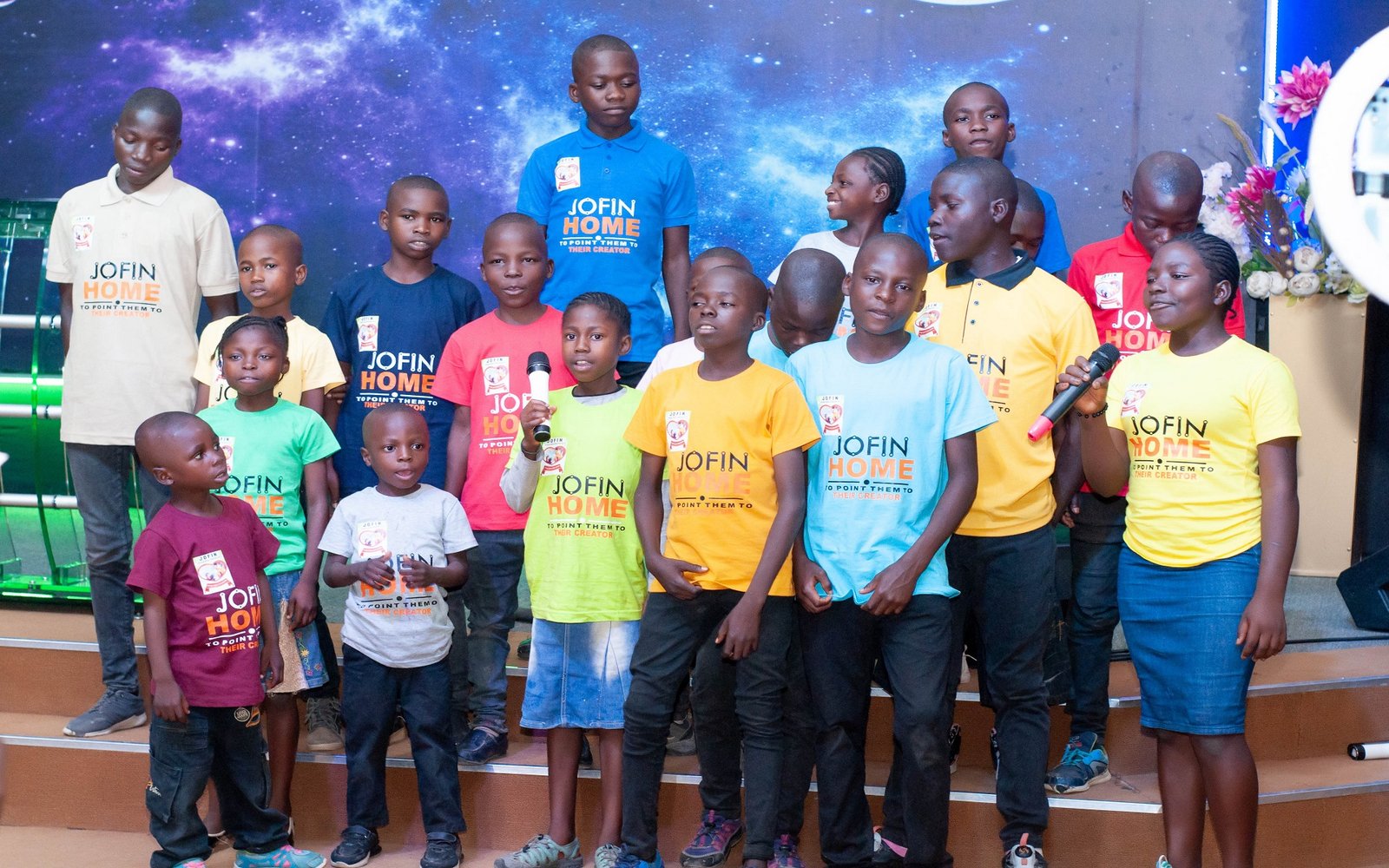 Children of JOFIN Home standing together on stage in JOFIN T-shirts