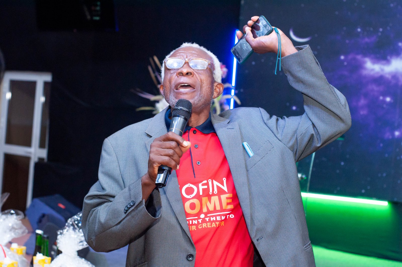 An older man in a JOFIN Home T-shirt speaking passionately into a microphone