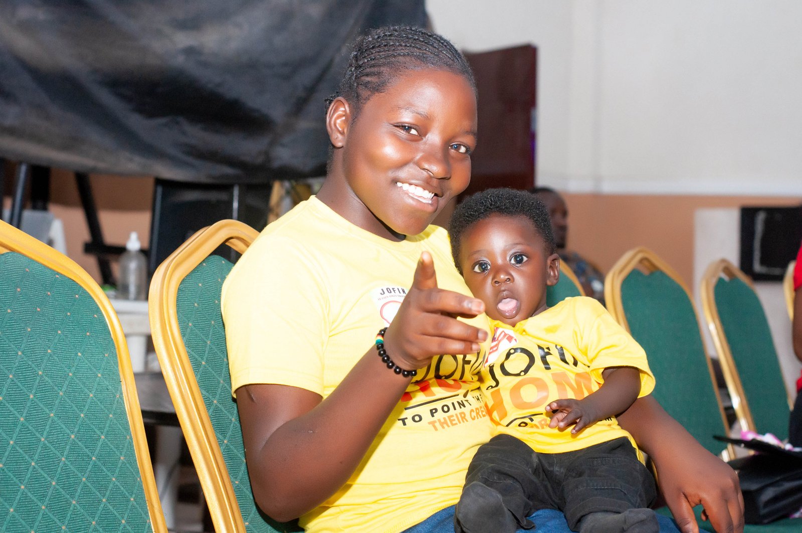 A girl in a JOFIN T-shirt smiling as she holds a younger child on her lap