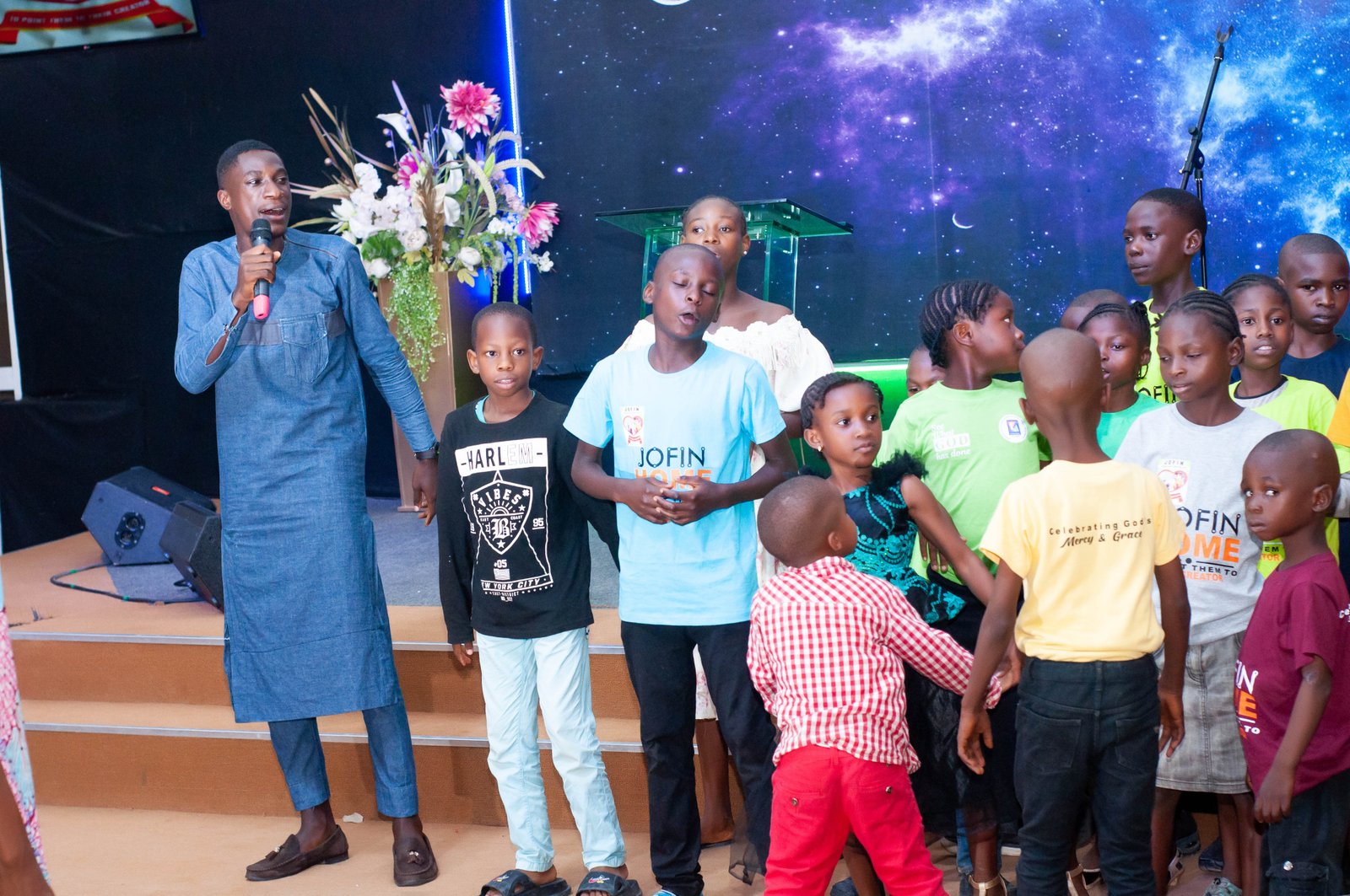 A young woman speaking to a group of children gathered on a stage