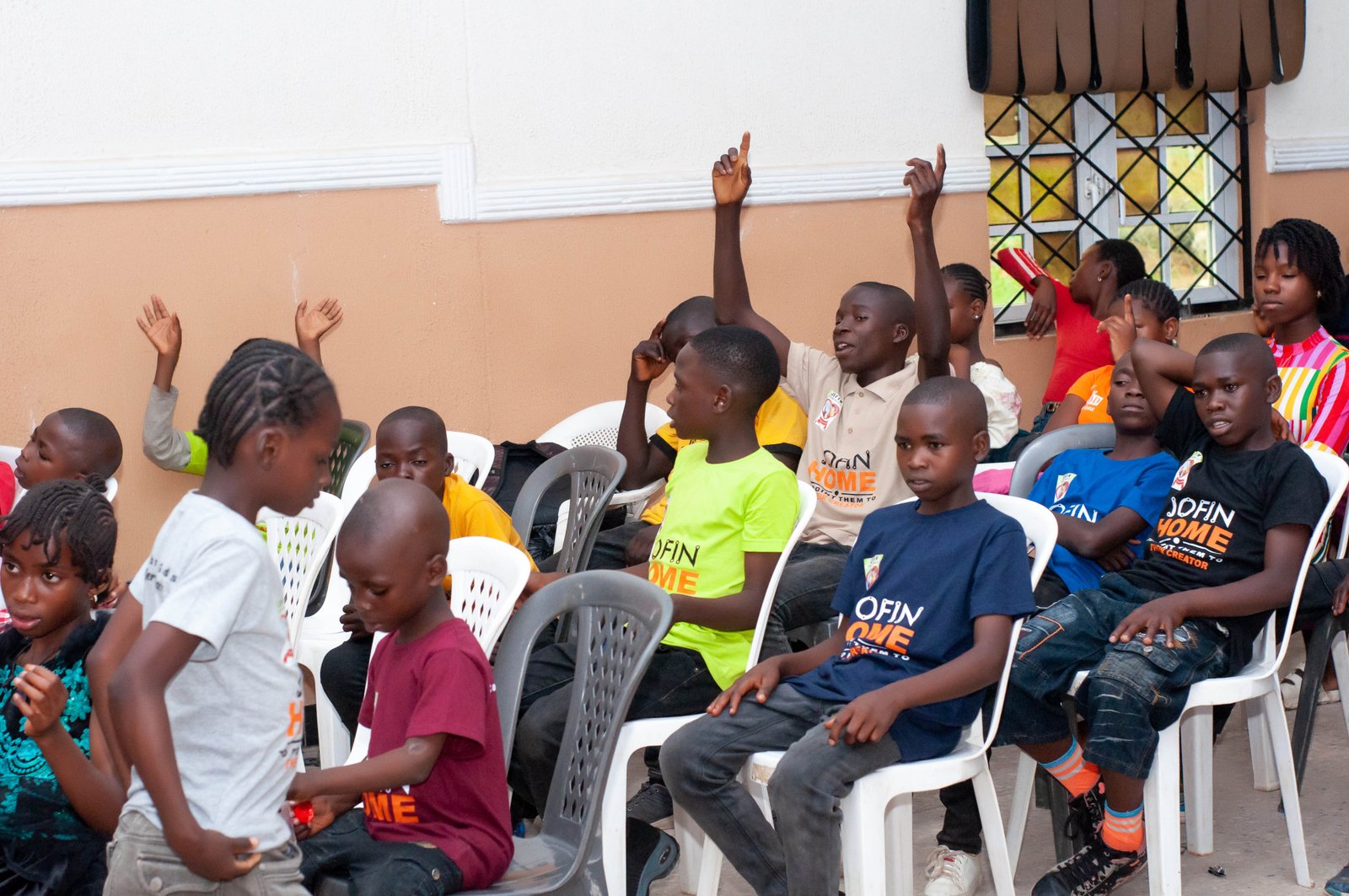 Children seated in rows, several raising their hands to answer a question