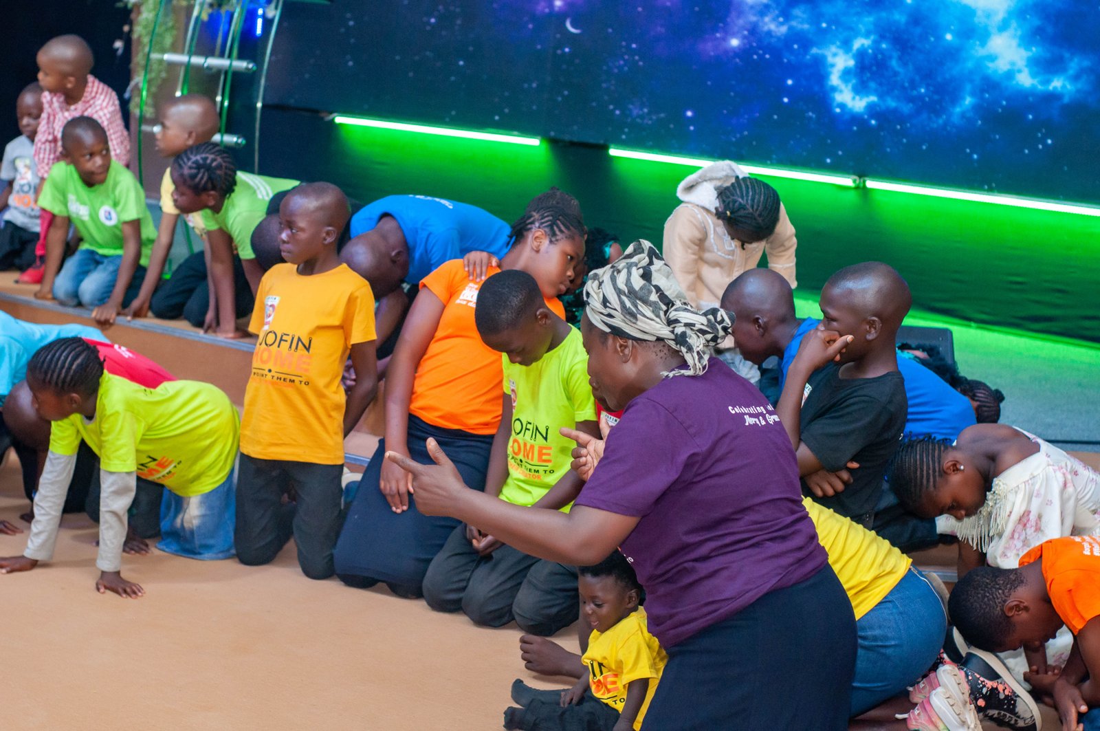 A caregiver praying with children kneeling around her