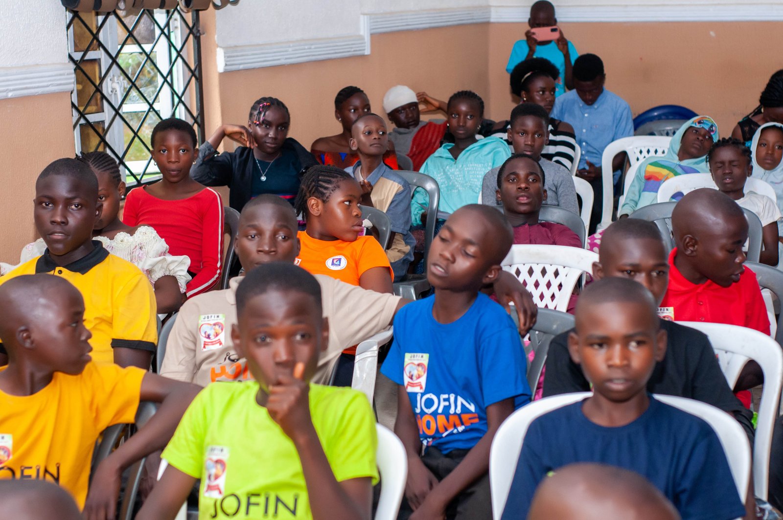 Children in JOFIN T-shirts seated and listening attentively